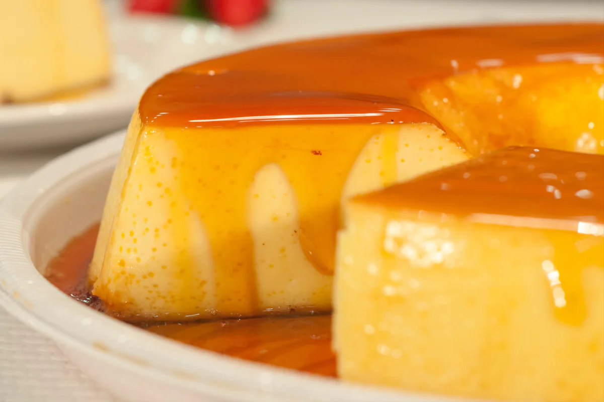 Pudim de leite cremoso com calda escorrendo em uma bandeja de para doces coberta com calda